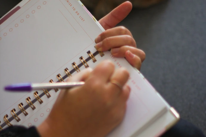 a person writing on a notebook next to a dog